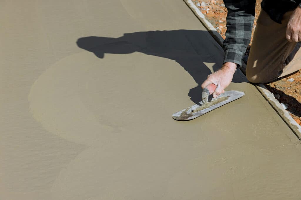 a worker smooths freshly poured concrete with a metal tool